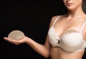 Woman wearing a bra holding a breast implant in her hand