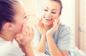 Young woman looking in the mirror and touching her face enjoying her clean skin