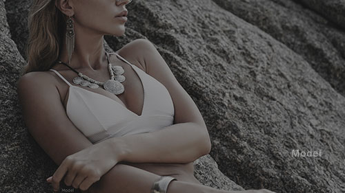 Mid body shot of a woman in a bikini top laying back on a boulder