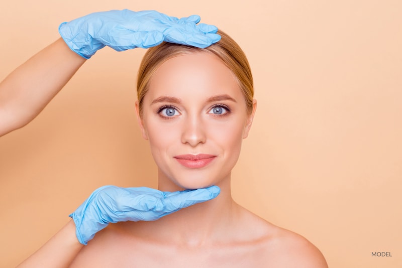 Woman on peach background with doctor's hands surrounding her face