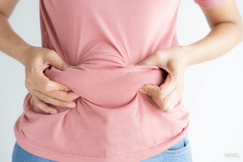 Woman grabbing her excess belly fat through her pink shirt.