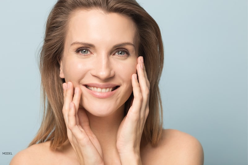 Woman touching her face against a light blue background.