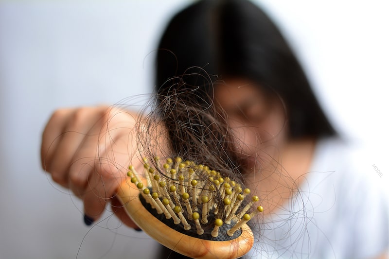 Young woman holding out a hair brush with hair strands tangled up on brush.