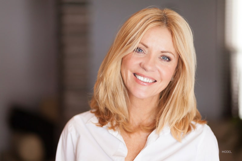 Middle-aged blonde woman wearing a white button-up shirt, smiling.