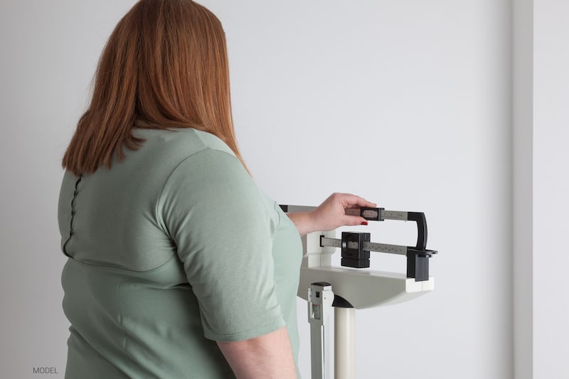Overweight woman standing on a medical scale and adjusting the weight