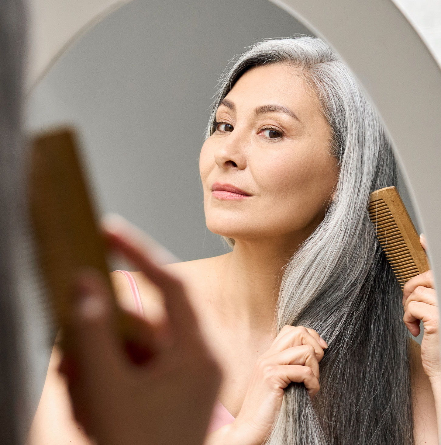Beautiful older woman looking into a mirror while brushing her hair